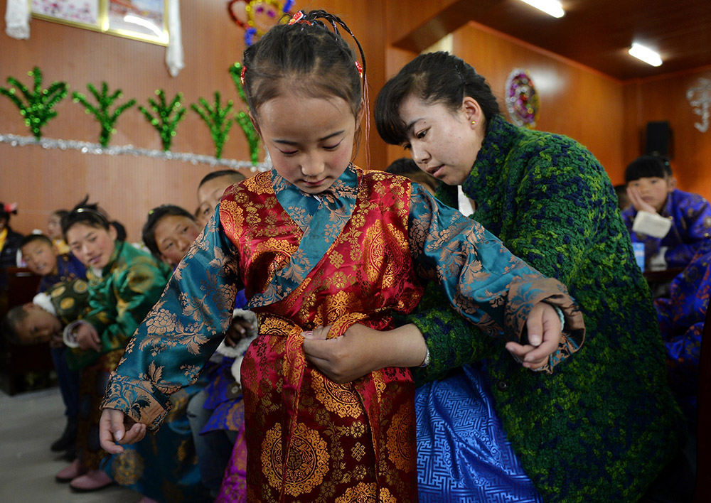 2月27日，在西藏自治區(qū)兒童福利院，來(lái)自拉薩市尼木縣的“愛(ài)心媽媽”德慶旺姆（右）在為來(lái)自那曲地區(qū)的嘎瑪曲宗換上節(jié)日盛裝。